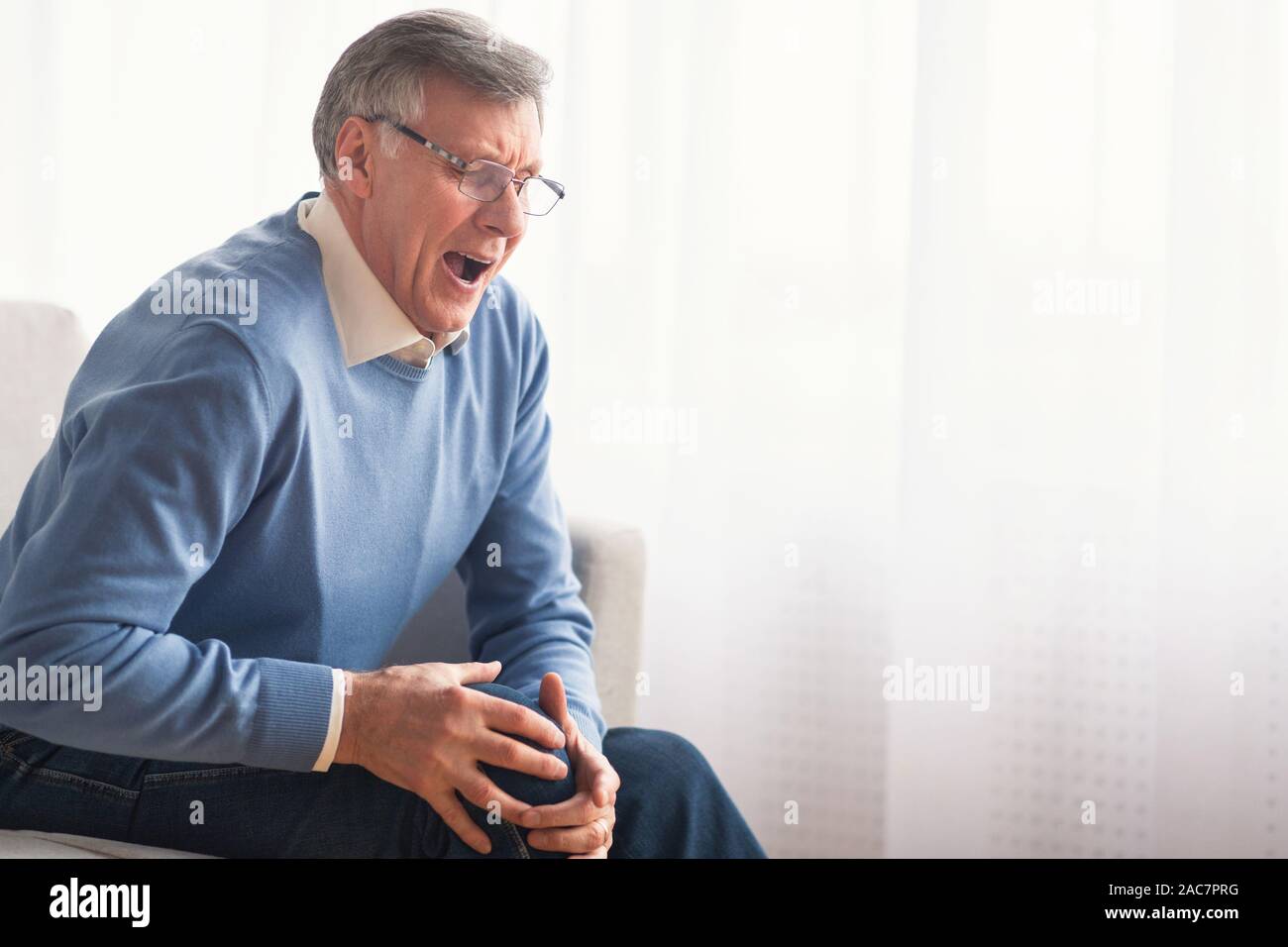 Senior gentleman having knee pain sitting on sofa at home Stock Photo