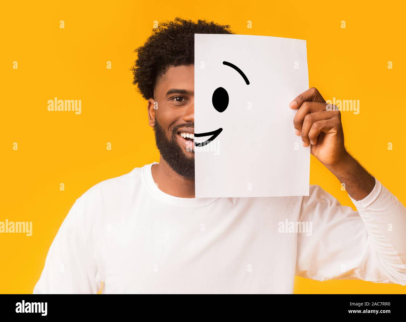 Black cheerful man covering half face with smiley picture Stock Photo