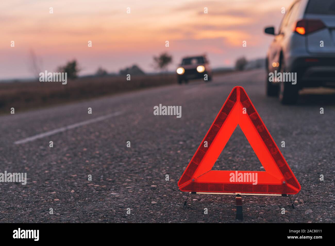 Warning triangle sign on the road in sunset by the broken car, selective focus Stock Photo