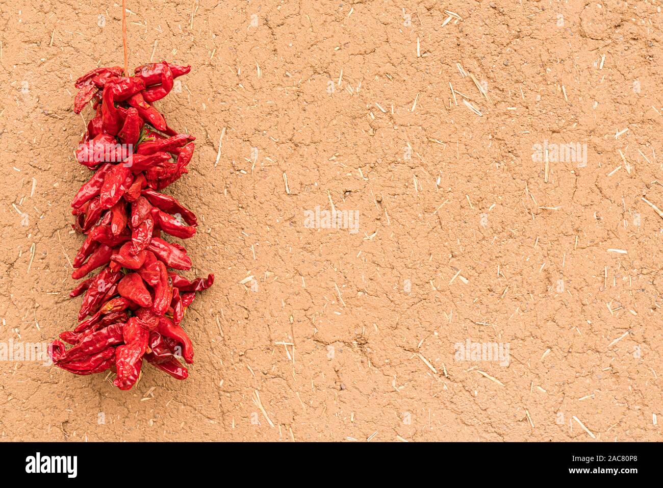Dried red chili peppers hanging on the exterior of adobe Wall Stock Photo