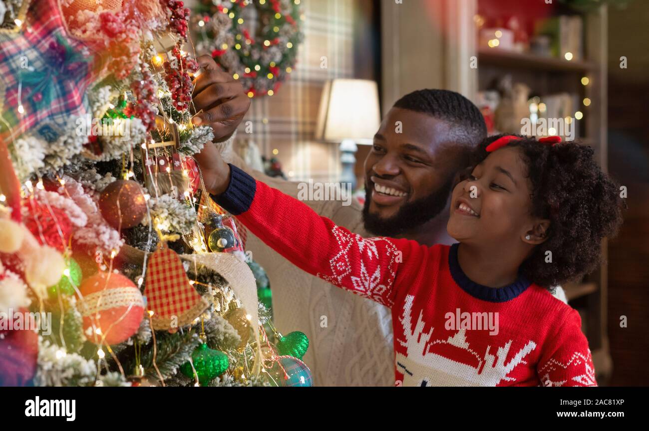 Little afro girl helping daddy to decorate family Christmas tree Stock ...