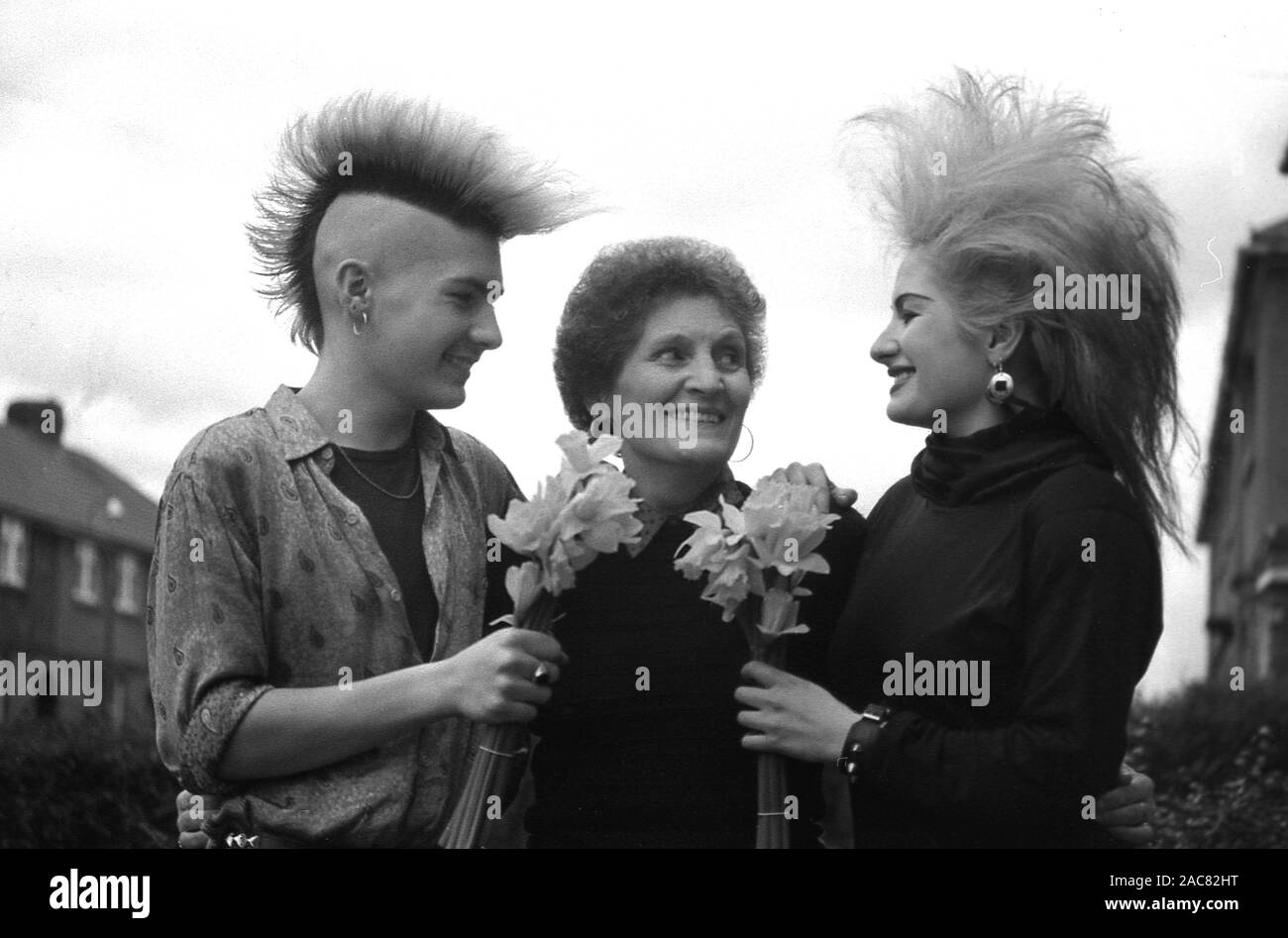 1987, 'mother's day'...two young adults in the 'punk' hair fashions of the era, standing outside in a street present their mother with flowers on this special day, England, UK. Stock Photo