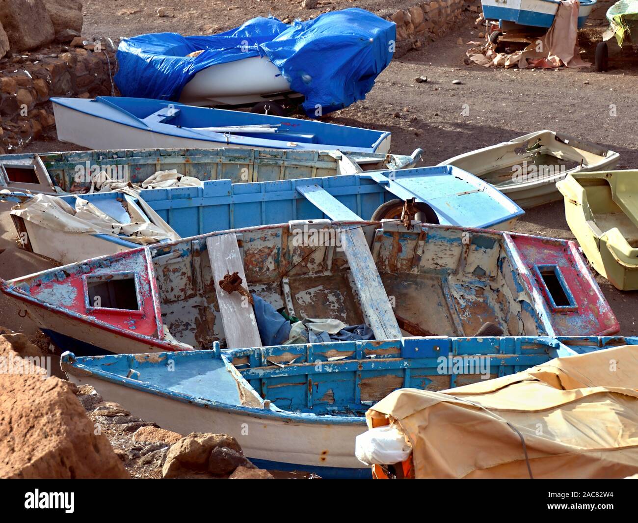 Small old and dilapidated wooden fishing boats close to each other on the beach. The colors are flaked off and the varnish is off. Stock Photo
