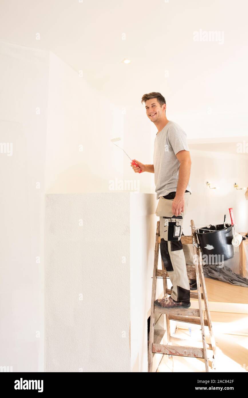 Shot of professional contractors standing on ladder and painting wall while refurbishing the apartment. Stock Photo