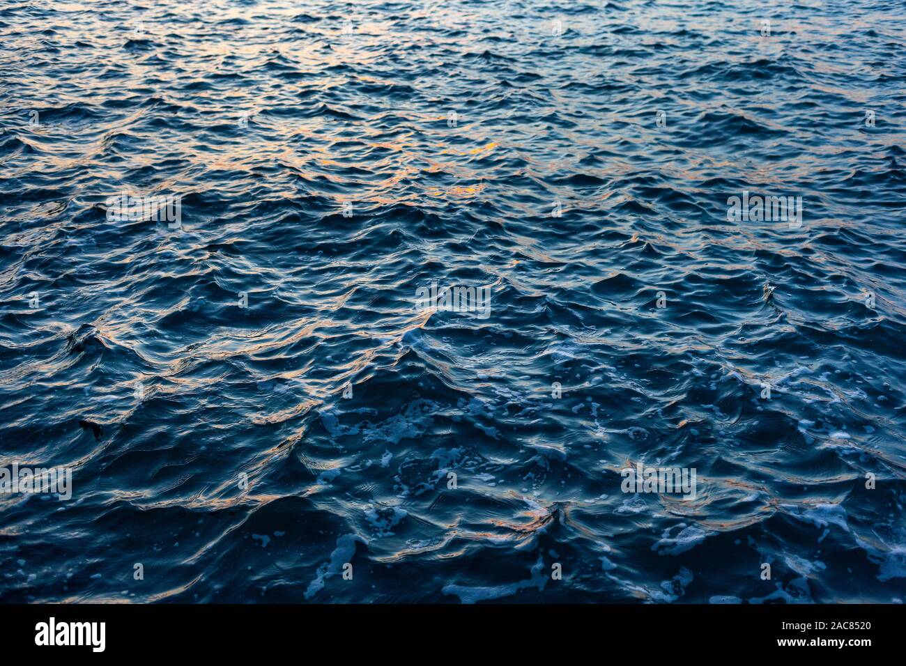 Dark blue Sea water with a choppy  texture and reflected orange highlights from a sunset Stock Photo