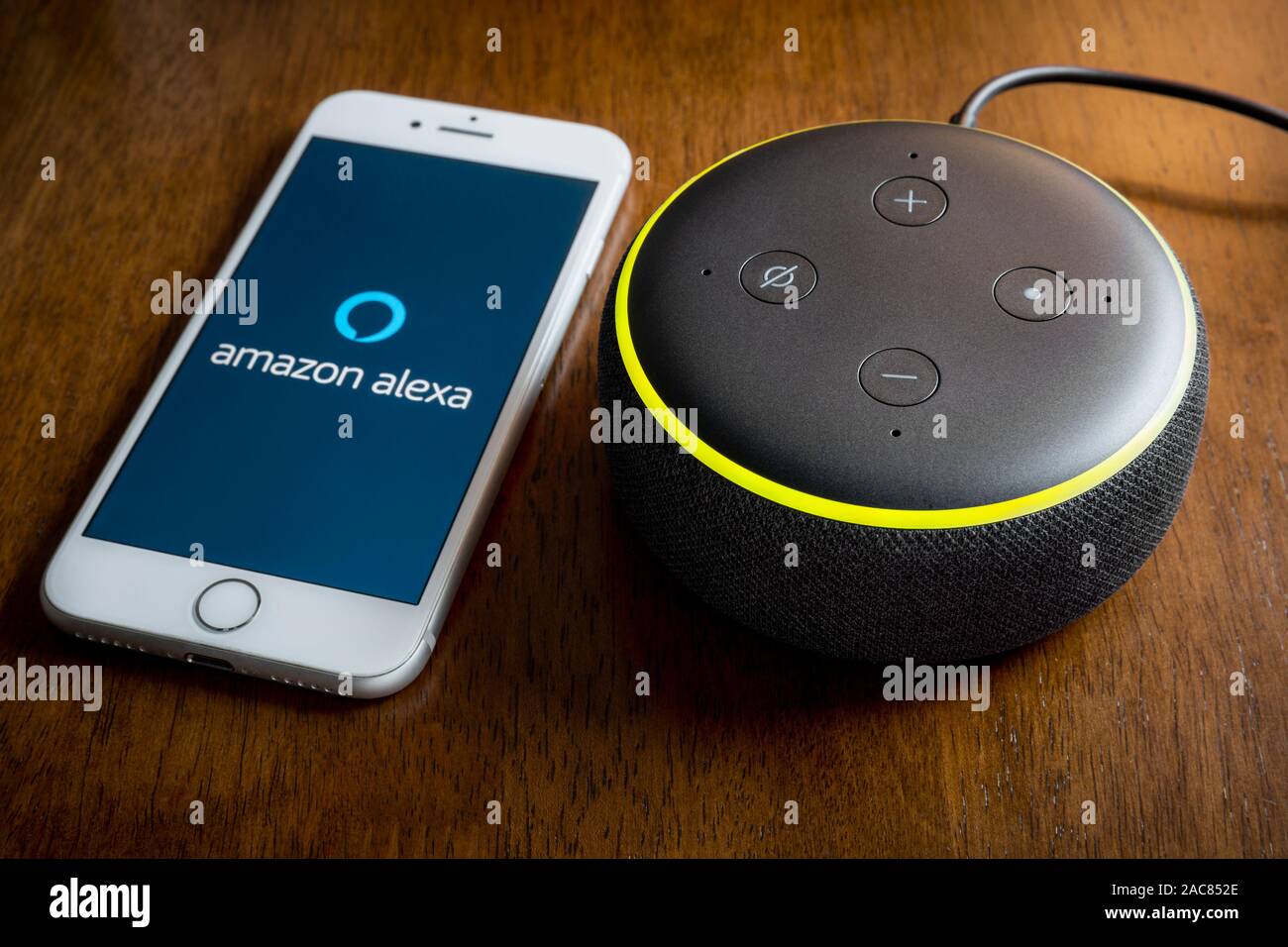 BATH, UK - DECEMBER 1, 2019 : Close up of an 3rd generation Amazon Echo Dot on a desk next to an Apple iPhone running the Amazon Alexa Application Stock Photo