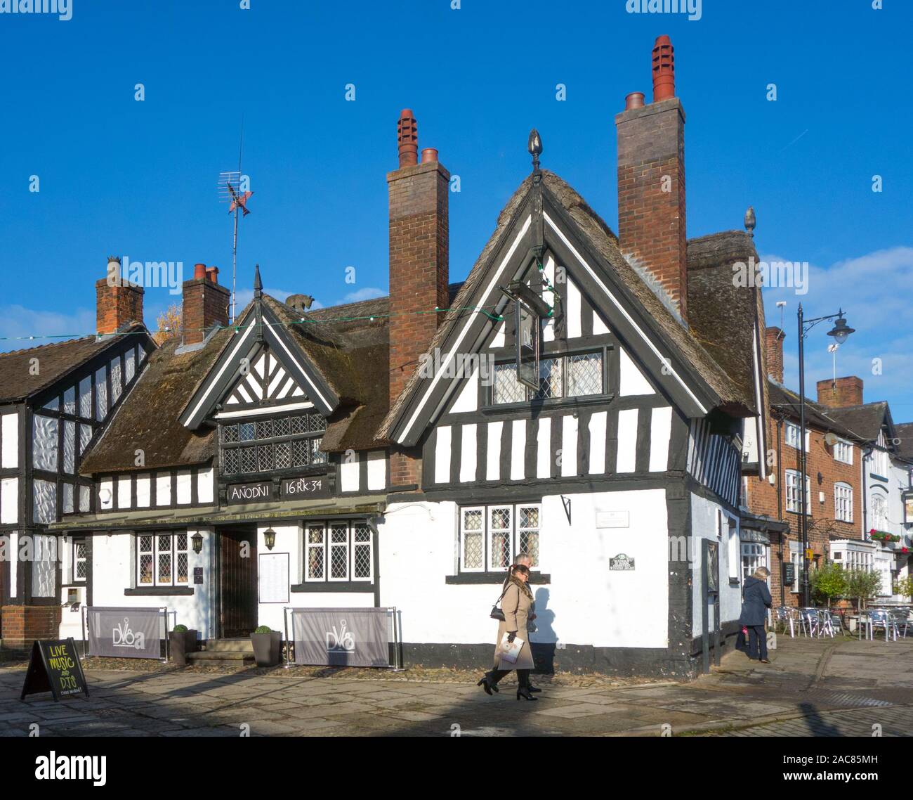 Man and woman walking past the thatched roofed Black Bear inn public house in the market square in the Cheshire town of Sandbach Stock Photo