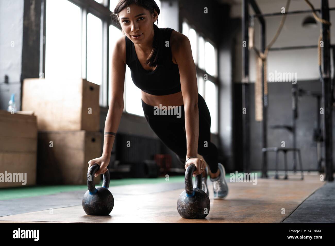 Slim brunette doing push-ups exercises on kettlebells. Cross fit training Stock Photo