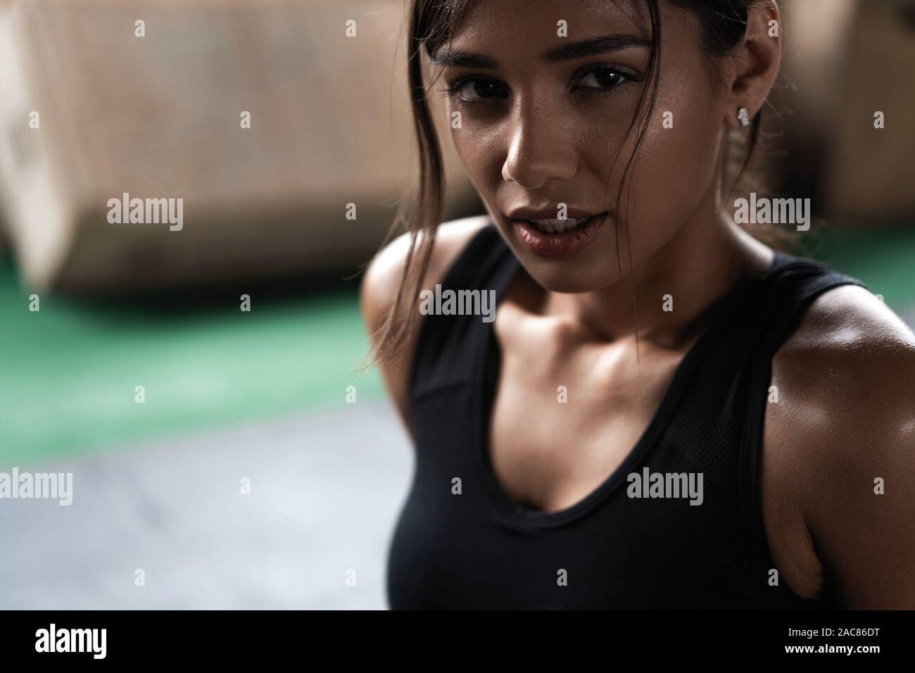 Young woman sitting on floor after her workout and looking down. Female athlete taking rest after fitness training Stock Photo