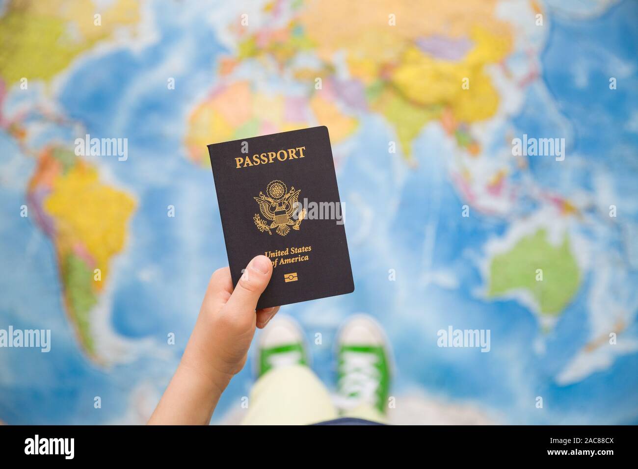 Child's hand holding US passport. Map background. Ready for traveling. Open world. Stock Photo