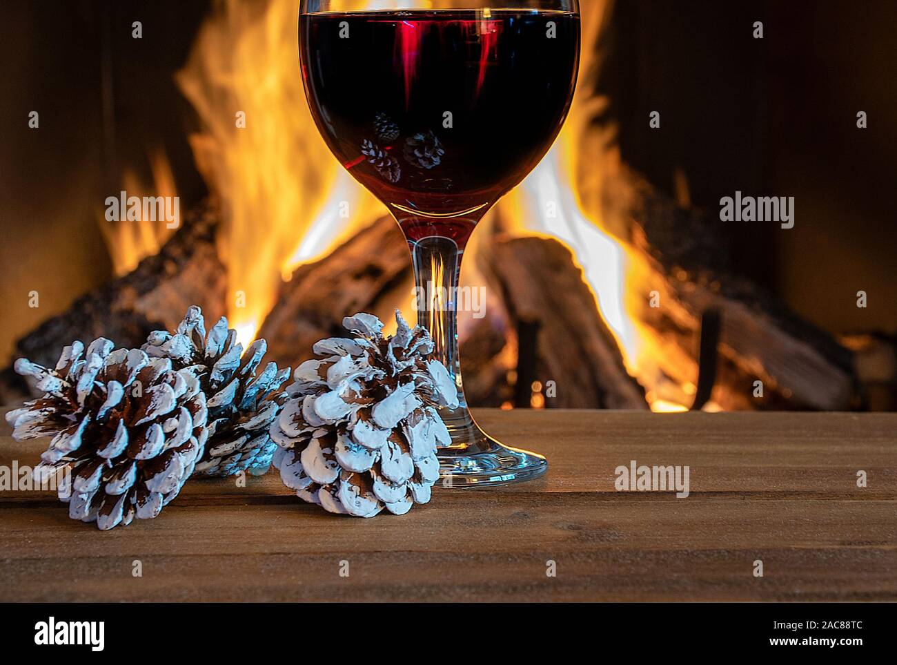 Glass Of Red Wine By Fireplace With Christmas Frosted Pine Cones