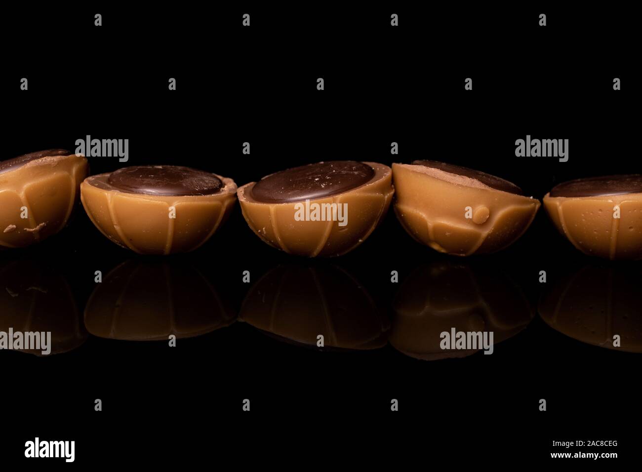 Group of five whole sweet brown toffee in line isolated on black glass Stock Photo