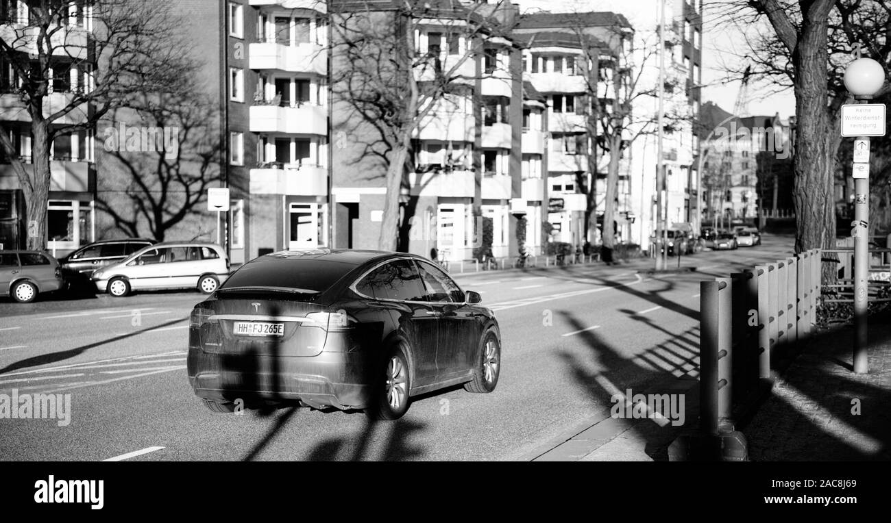 Hamburg, Germany - Mar 2018: Side view of black Tesla Model X electric car driving fast on German Bei den Muhren street with apartments buildings in background black and white image Stock Photo