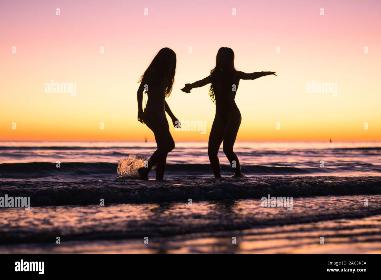 Two young girls dance during sunset in the ocean by the beach while on vacation Stock Photo
