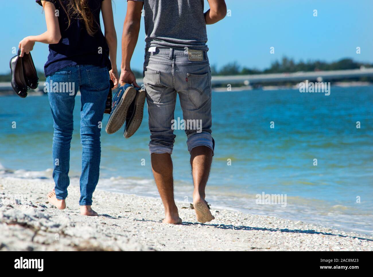 A couple walks down the beach in the summer without shoes on, barefoot
