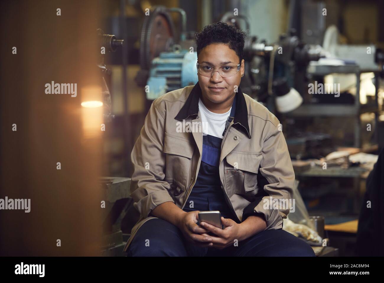 Portrait of contemporary mixed-race woman smiling at camera while posing in factory workshop Stock Photo