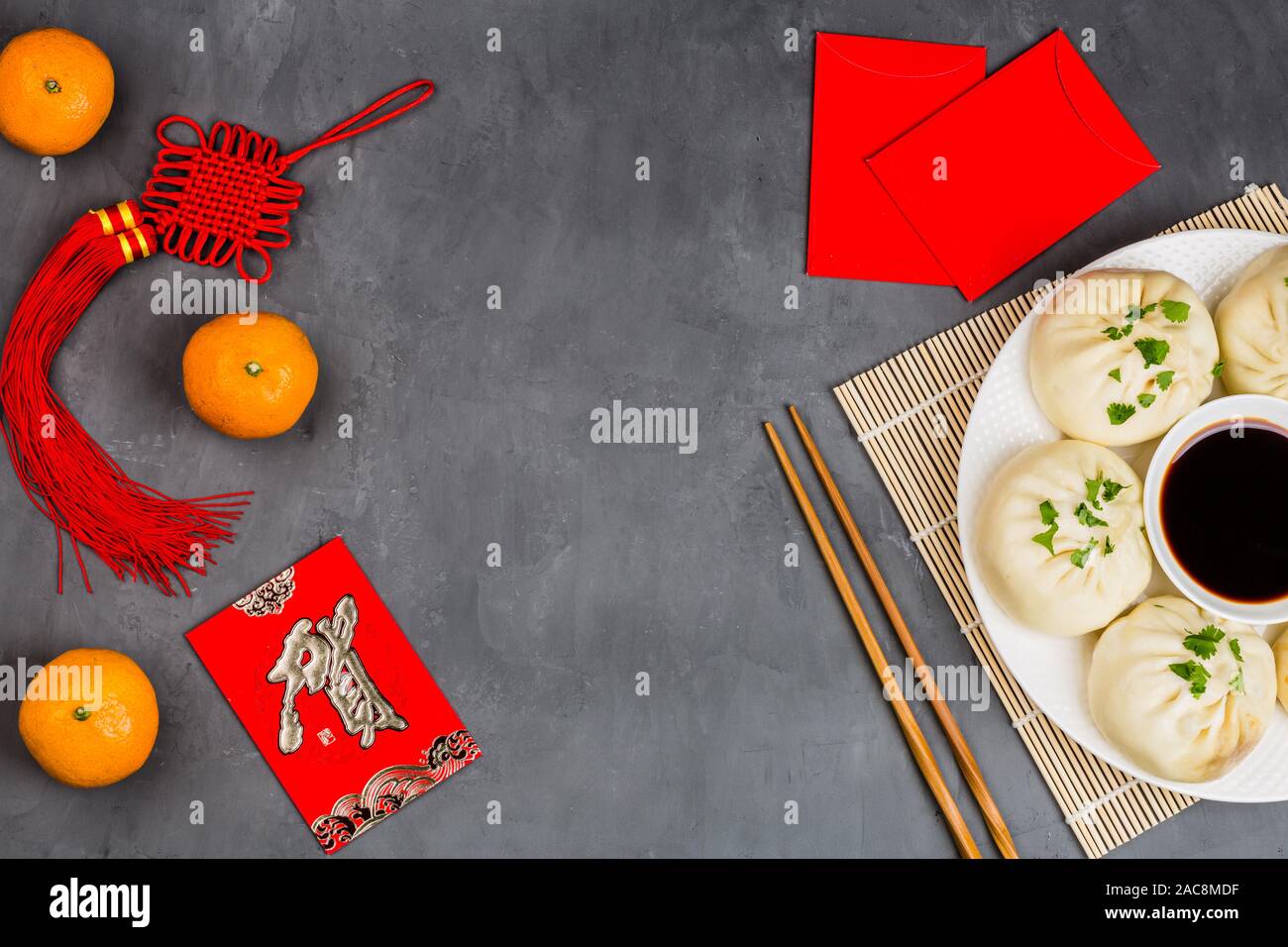 Chinese New Year decoration with dumplings, tangerines, soy sauce, chopsticks, red envelopes on gray concrete background. Happy Chinese new year 2020 Stock Photo