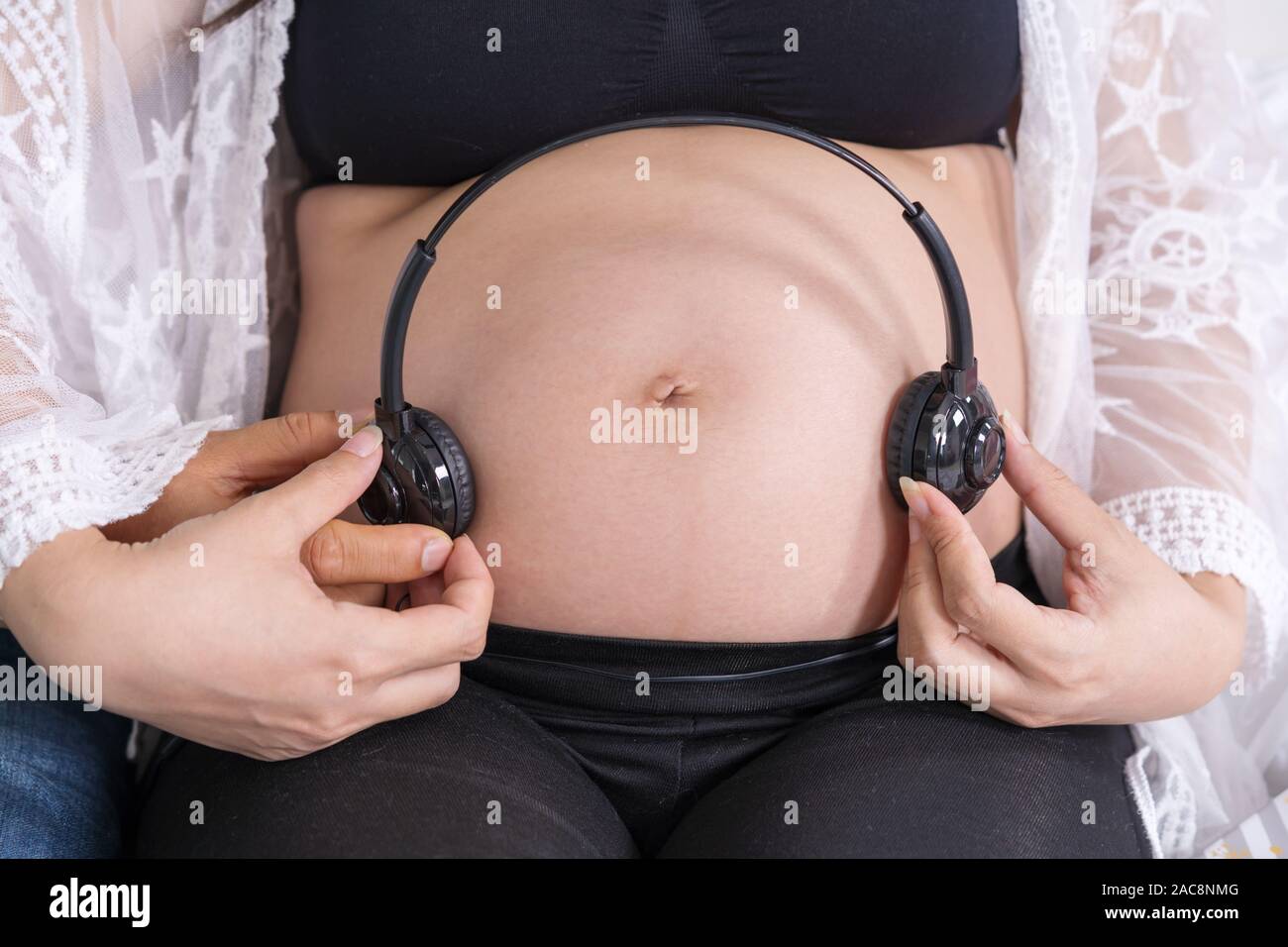 Pregnant woman holding headphones on belly, Stock image