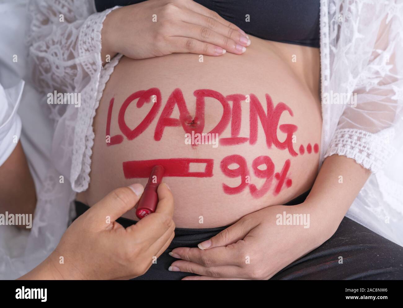 husband writting word 'loading 99%' on belly of his pregnant wife Stock Photo