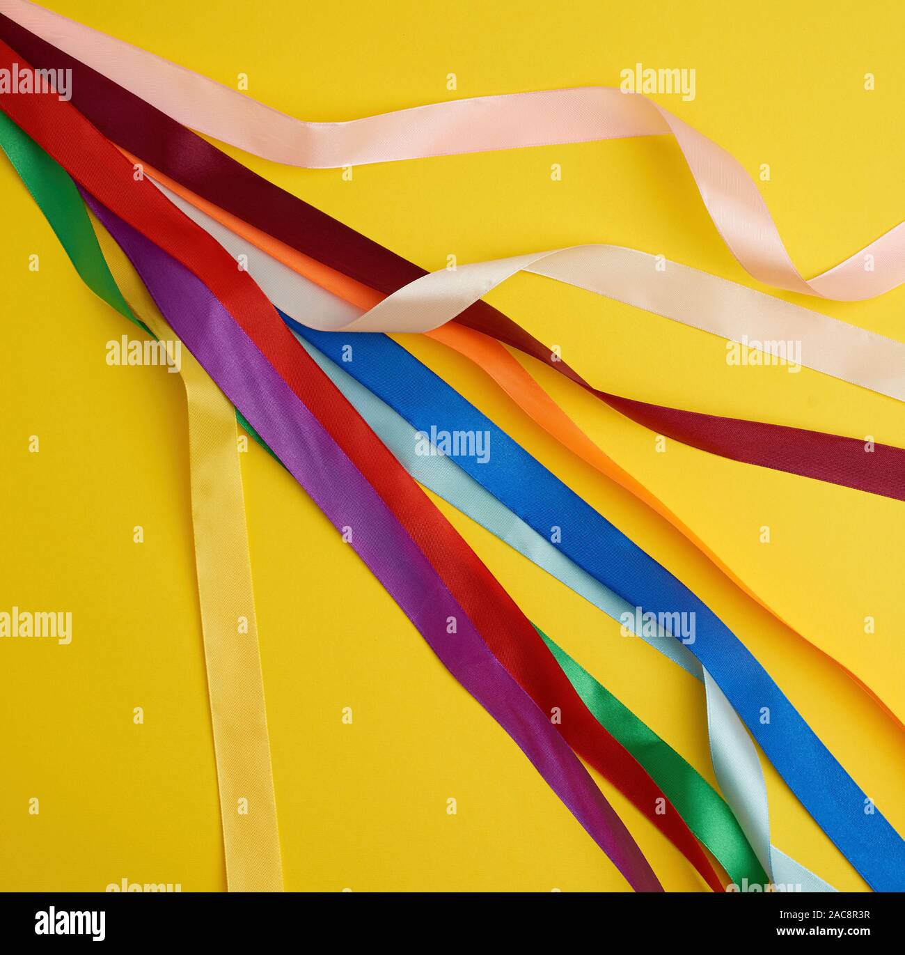 many silk multi-colored ribbons on a yellow background, top view Stock Photo