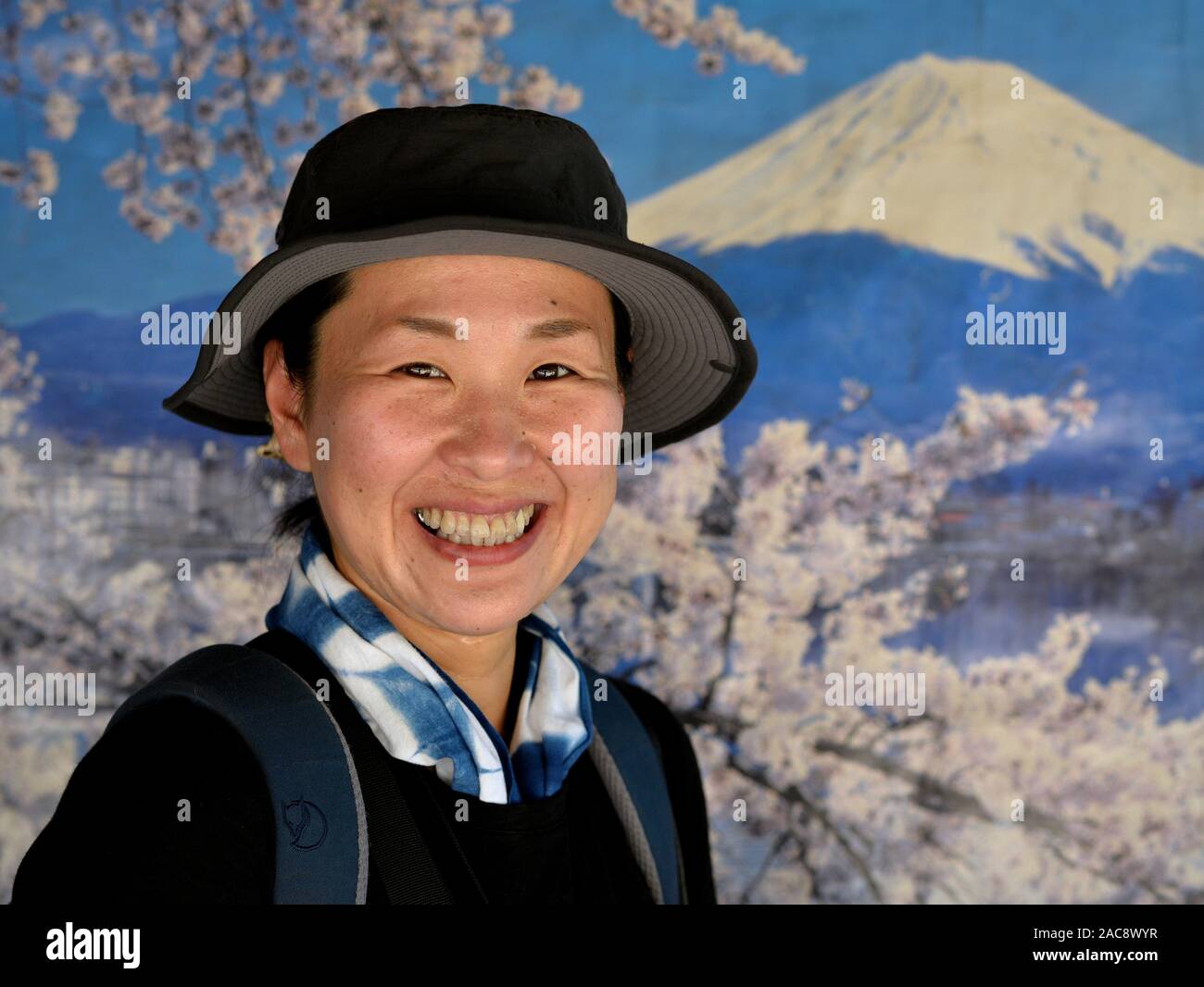 Japanese tourist smiles for the camera in front of an old Japanese tourism poster of Mount Fuji with cherry blossoms. Stock Photo