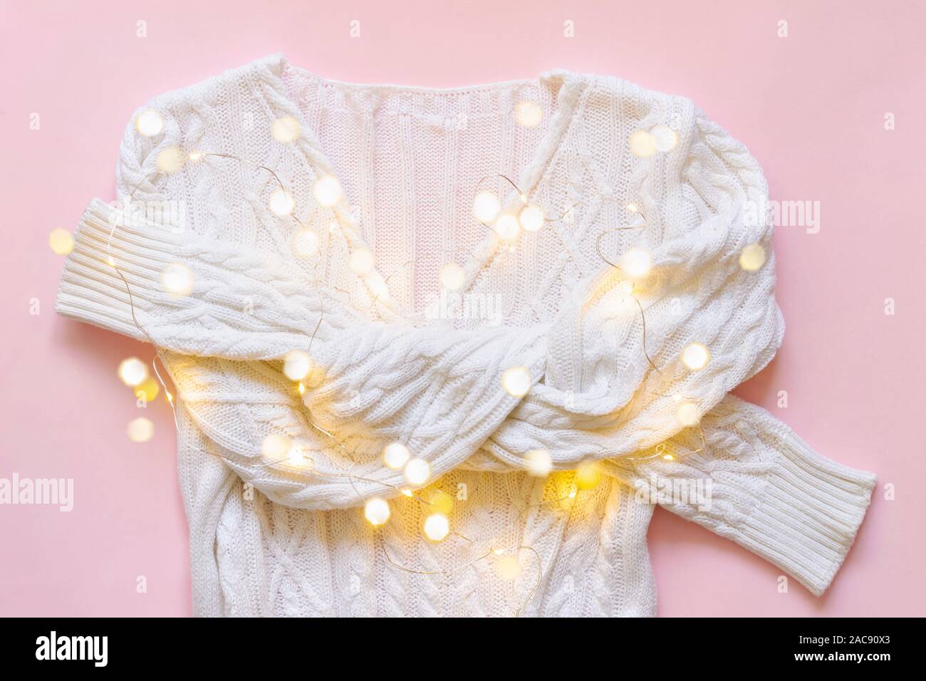 White knitted pullover with christmas light garland on pink background. Holiday concept. Stock Photo