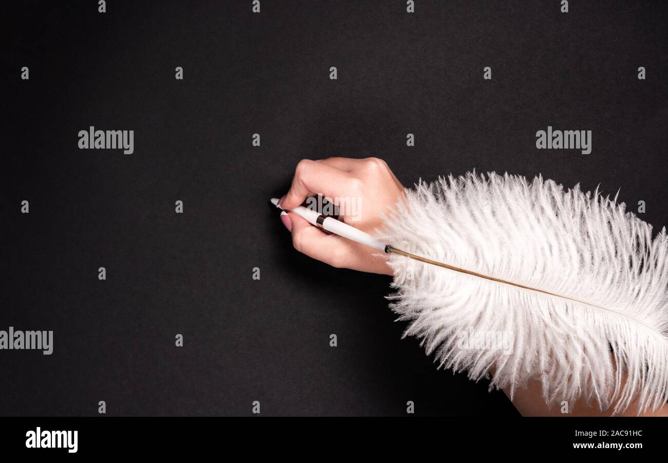 Female hand holding feather pen over black background Stock Photo