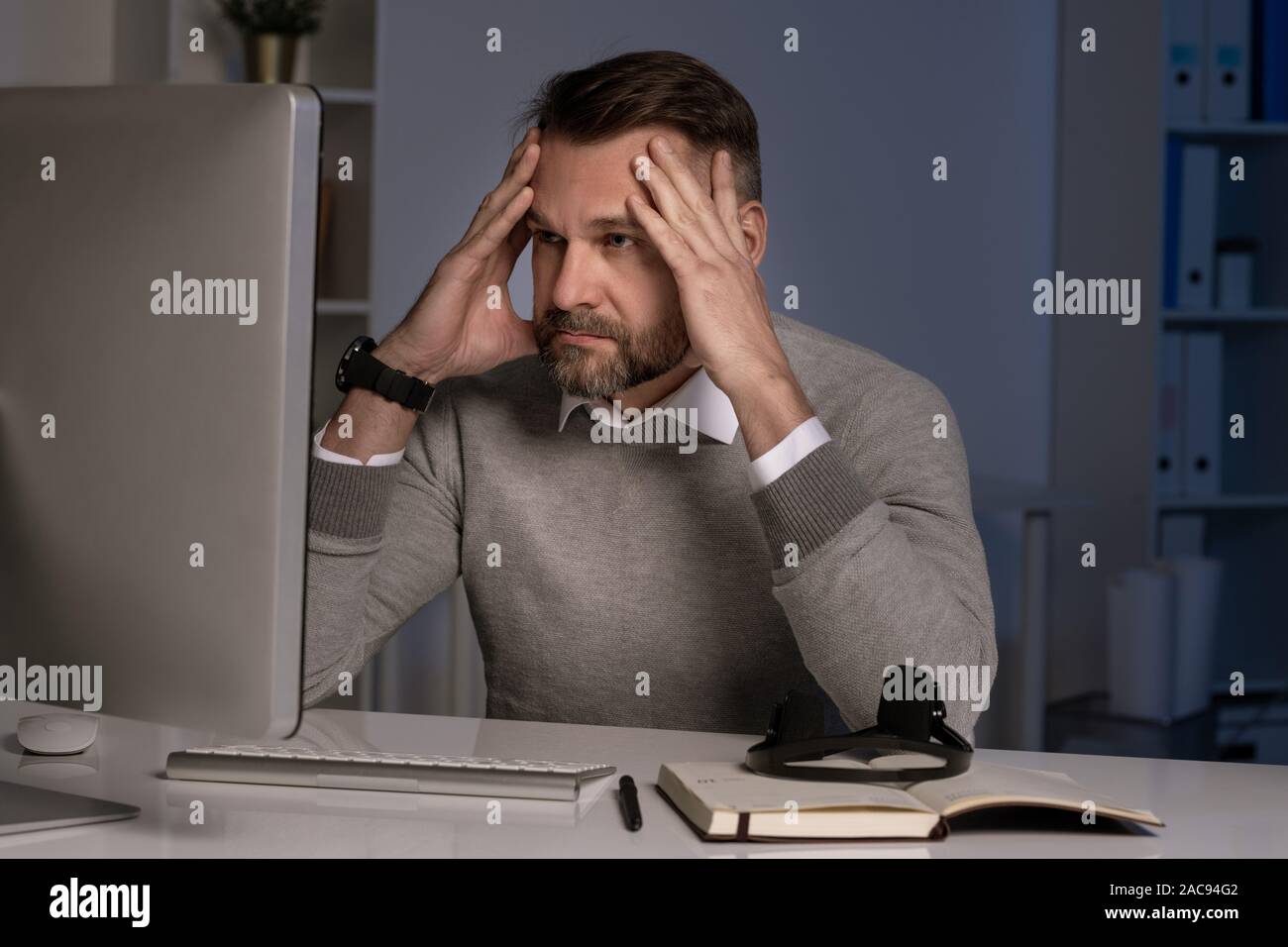 Serious and troubled office worker touching head while working in front of computer screen Stock Photo