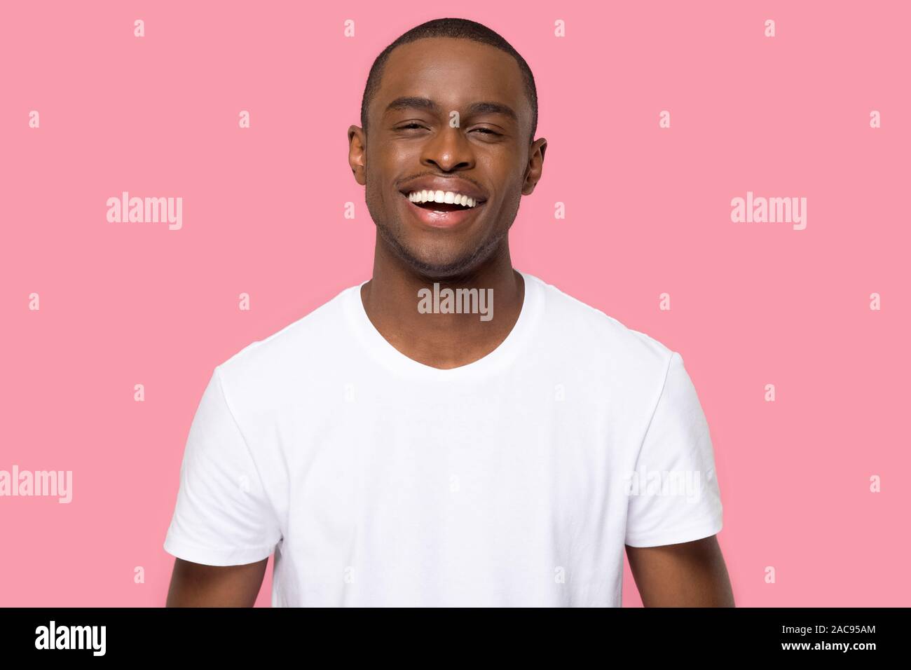 Head shot portrait African American man with beaming wide healthy smile looking at camera, handsome laughing young male, funny cheerful guy in white t Stock Photo