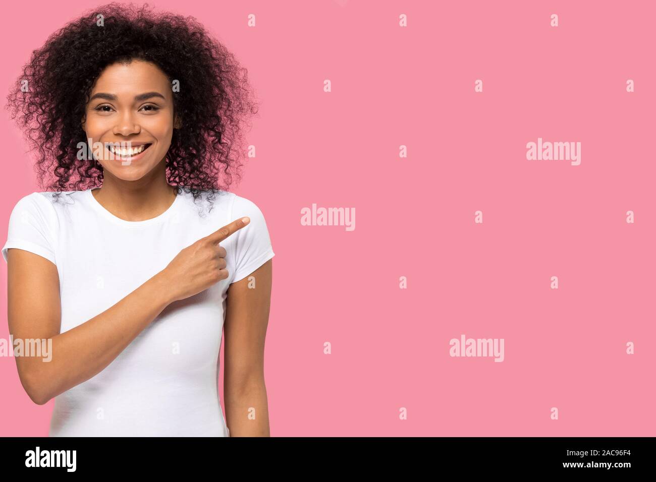Smiling African American woman pointing finger at pink copy space Stock Photo