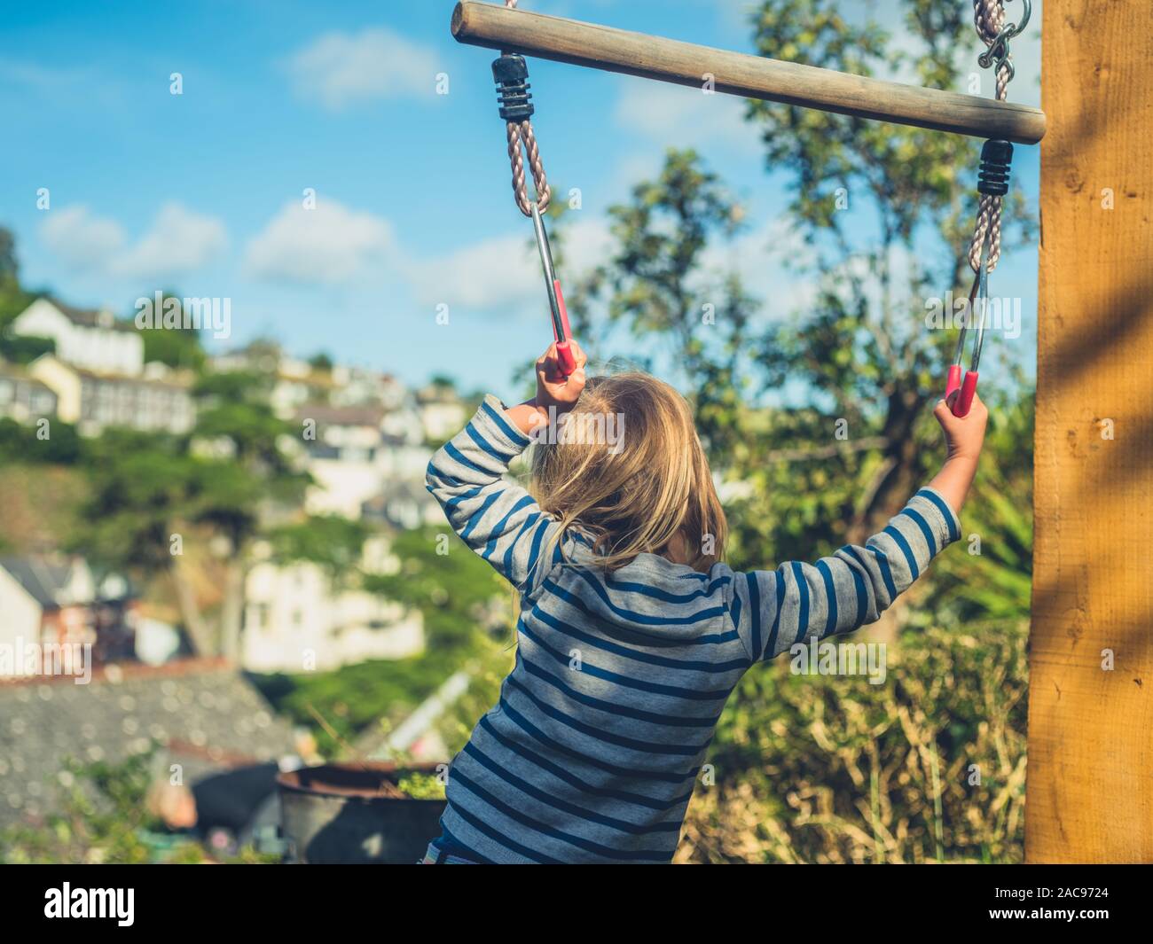 A little toddler is hanging from a trapeze in a garden in summer Stock Photo