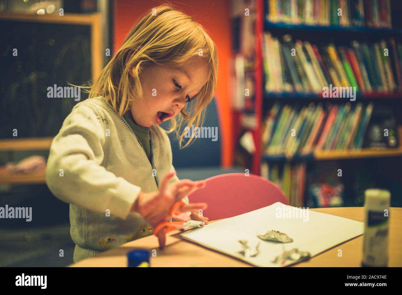 A little toddler is doing arts and crafts with scissors and glue at school Stock Photo