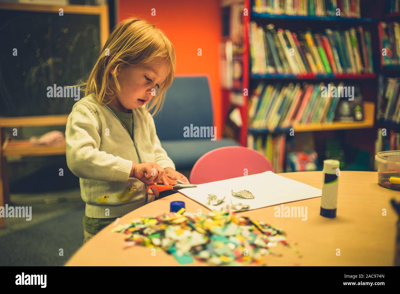 A little toddler is doing arts and crafts with scissors and glue at school Stock Photo