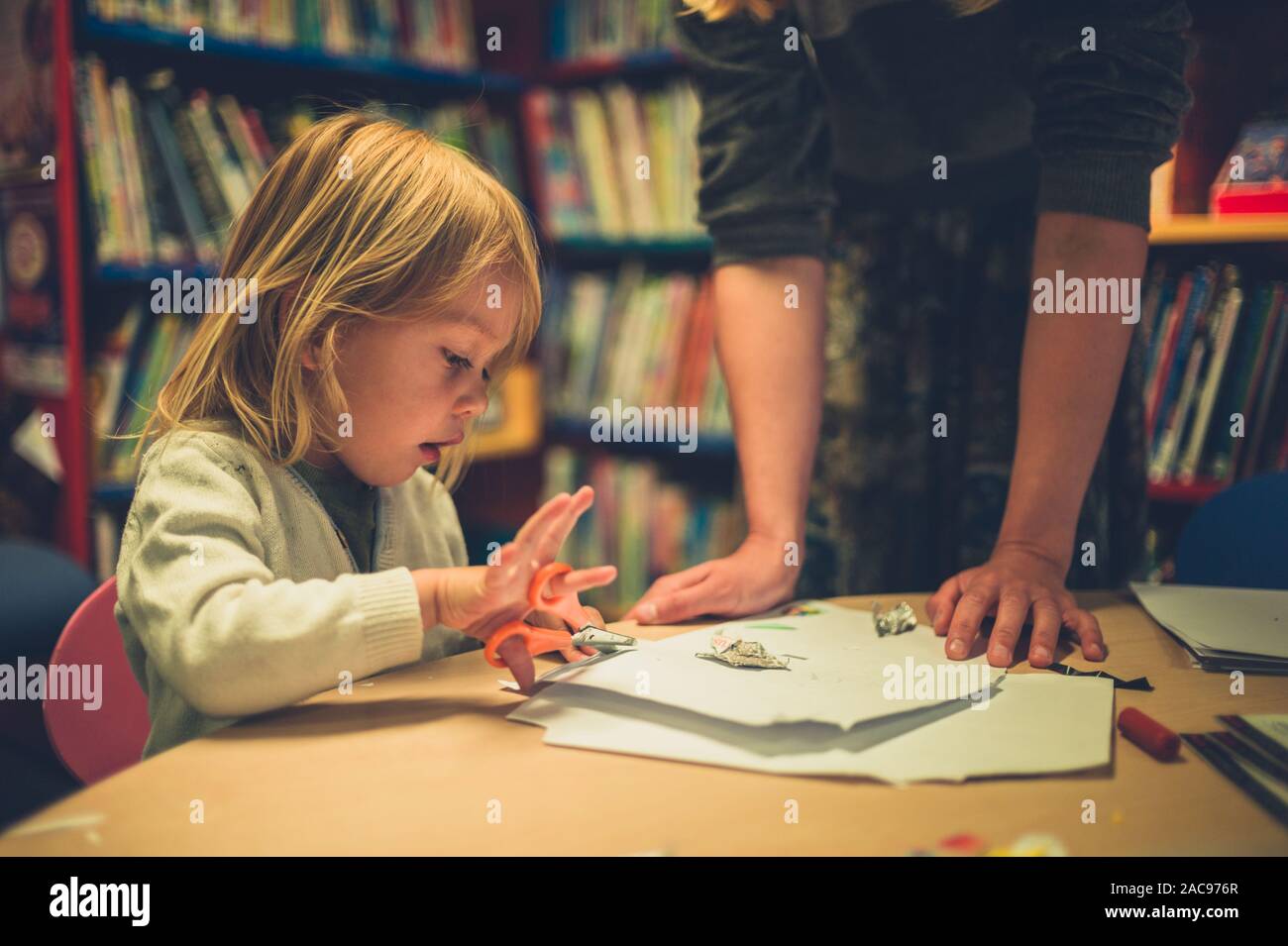 A teacher is supervising a little toddler using scissors at school Stock Photo