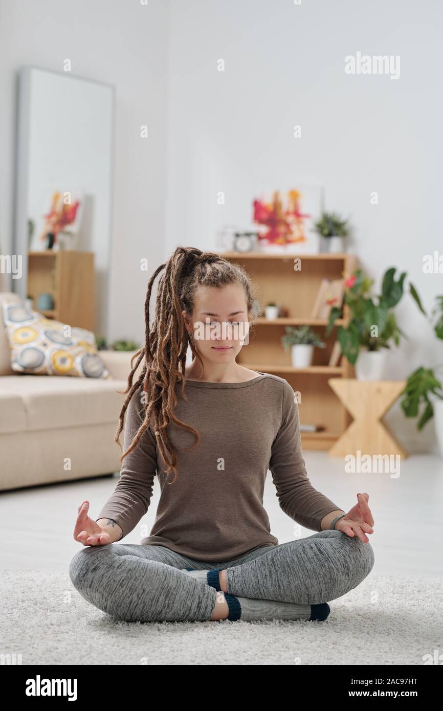Pretty young active woman with dreadlocks sitting on the floor with crossed legs Stock Photo