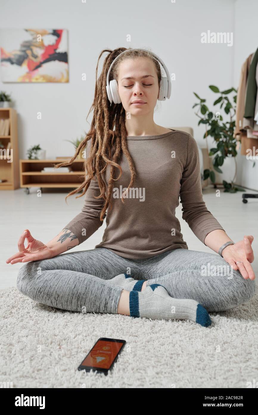 Serene girl in headphones sitting in pose of lotus and listening to relax music Stock Photo