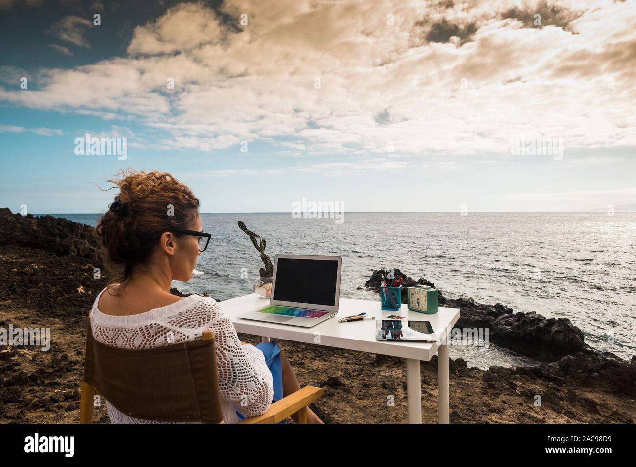 Modern and alternative lifestyle office wokstation with free business woman at work in open office with scenic ocean view - freedom from usual job - d Stock Photo