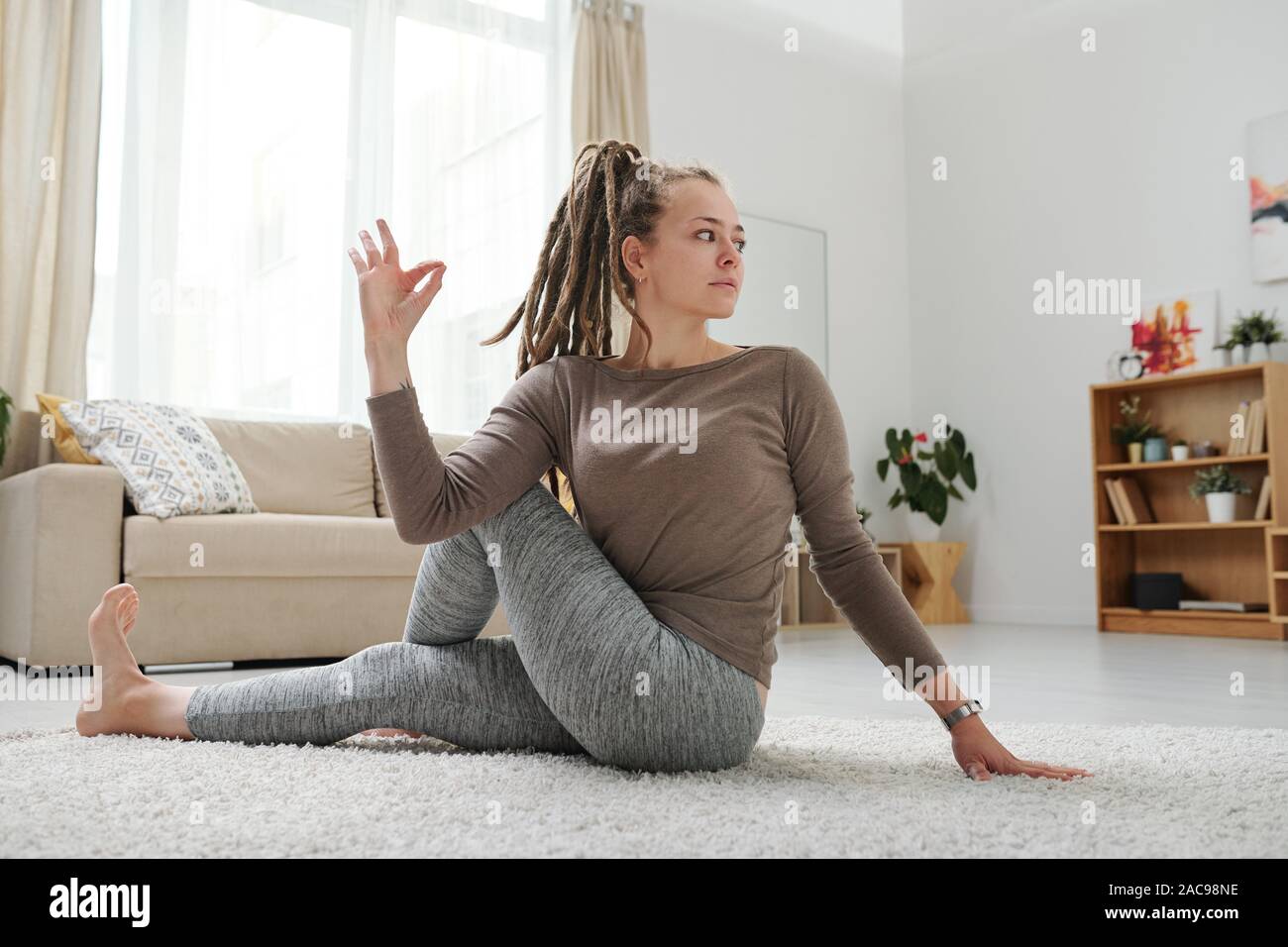 Young female with dreadlocks sitting on the floor in one of yoga positions Stock Photo