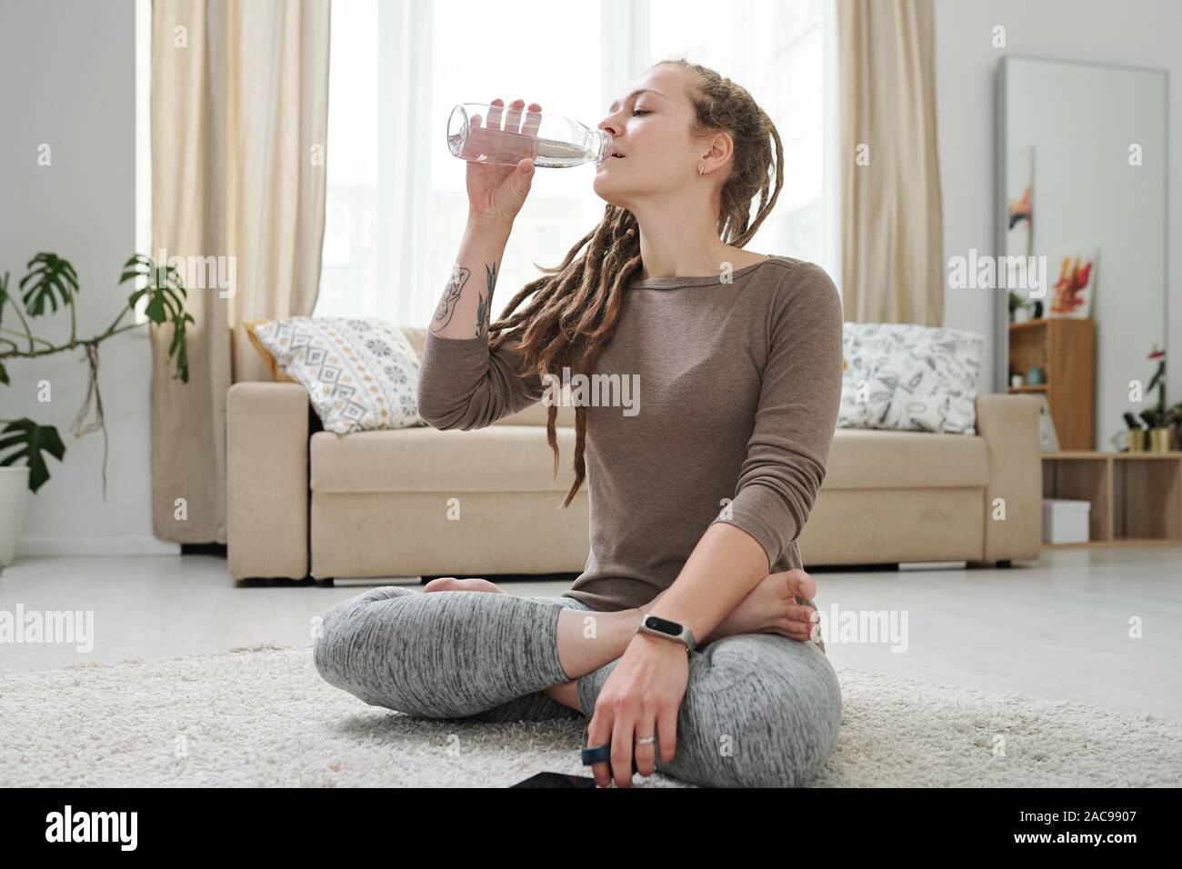 Thirsty young woman drinking water from bottle after workout at home Stock Photo