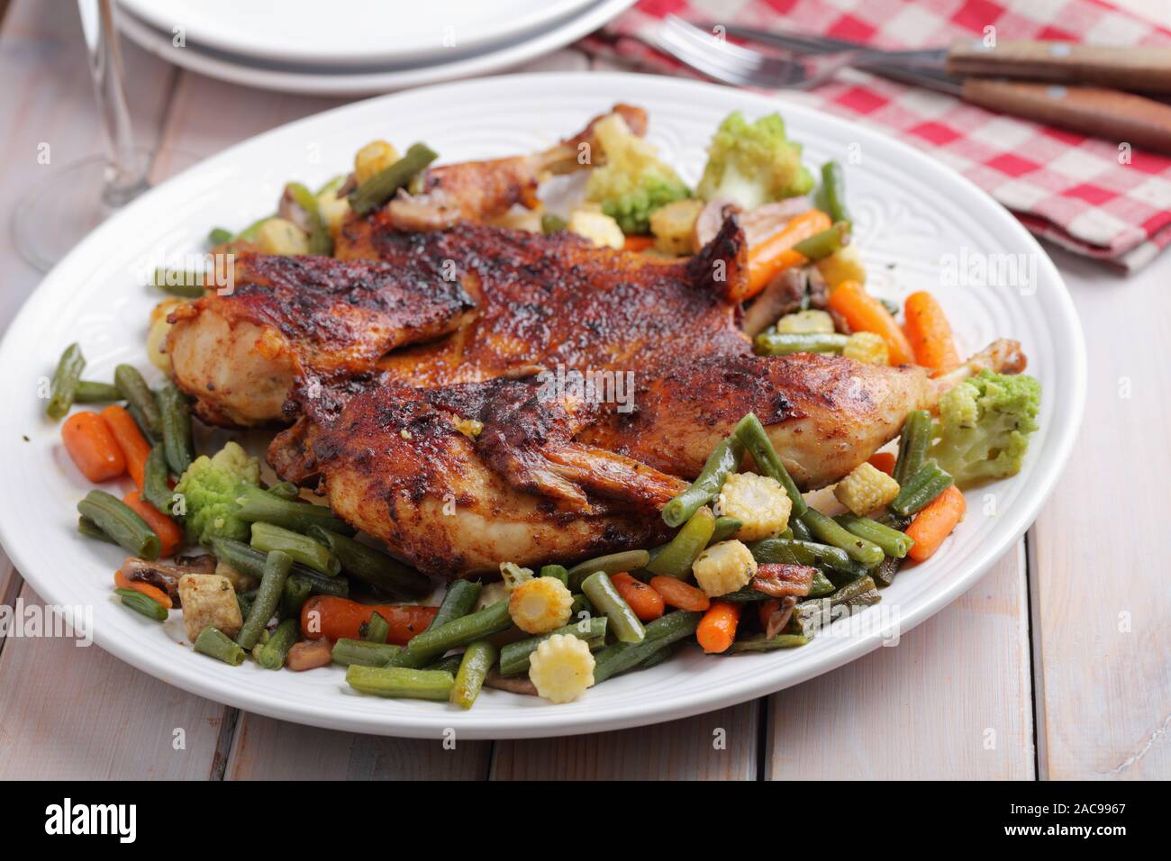 Chicken under a brick, or pollo al mattone, with roasted vegetables on a large white dish Stock Photo
