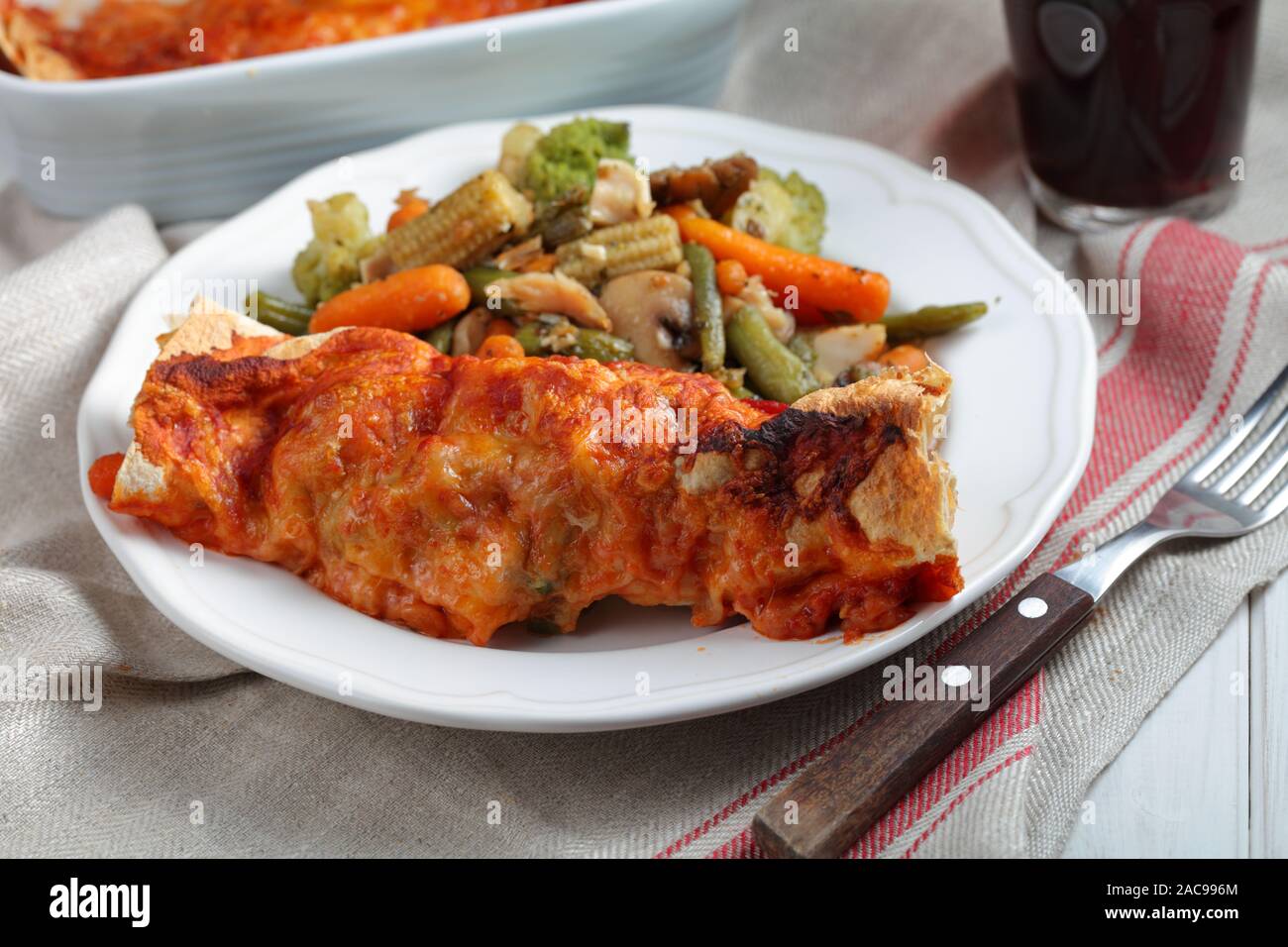 Two enchiladas in a baking dish with roasted vegetables and a glass of dark beer Stock Photo