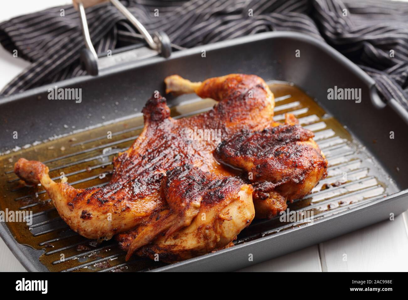 Cooking chicken under a brick, also known as brick chicken, or pollo al mattone, on a grill pan Stock Photo