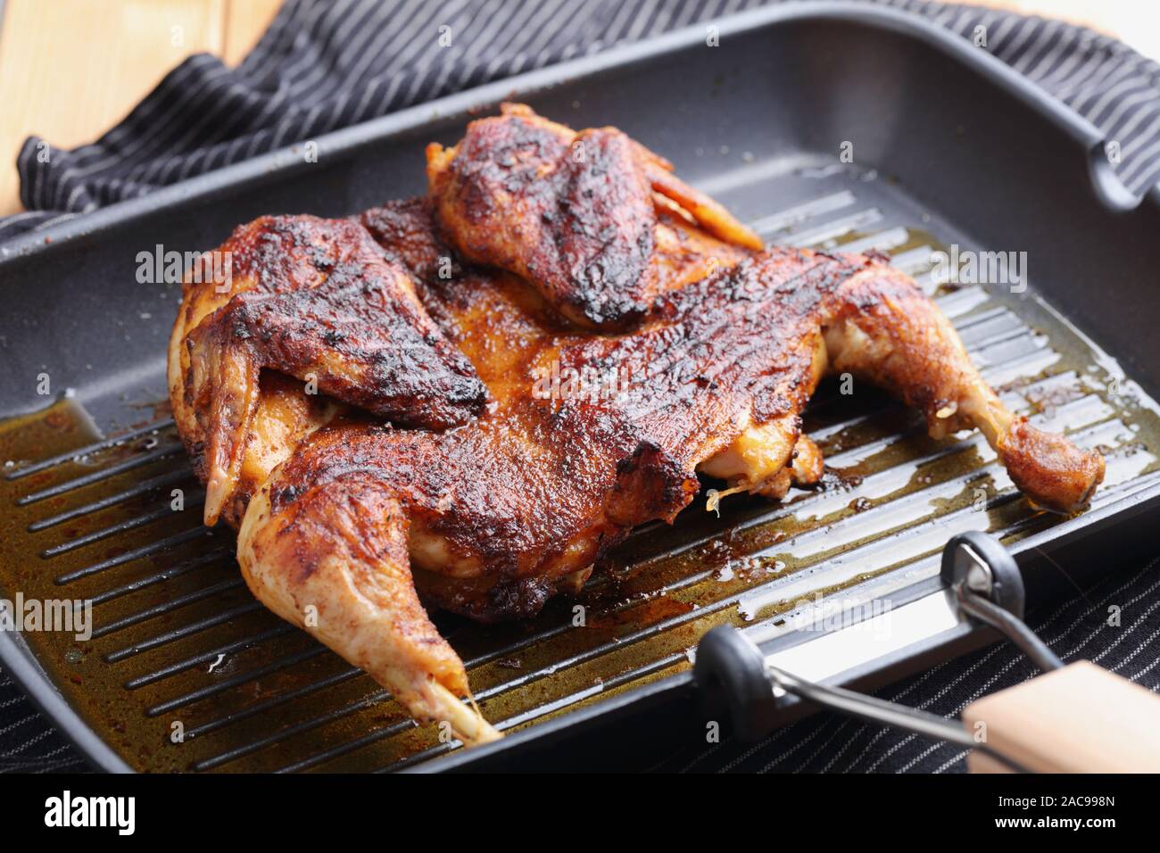 Cooking chicken under a brick, also known as brick chicken, or pollo al mattone, on a grill pan Stock Photo