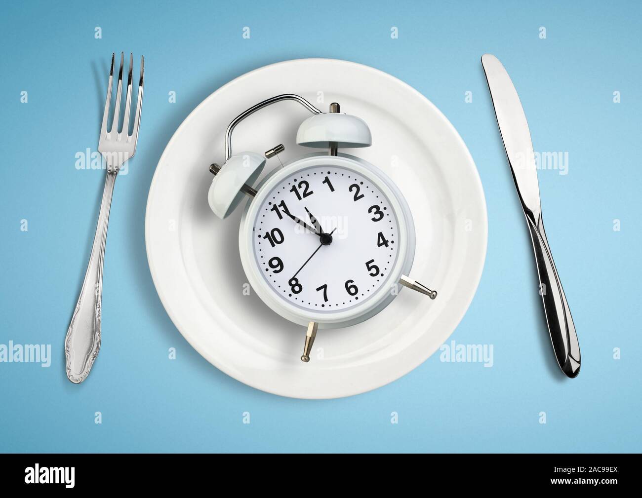 Concept of intermittent fasting, lunchtime, diet and weight loss. Clock on plate. Stock Photo