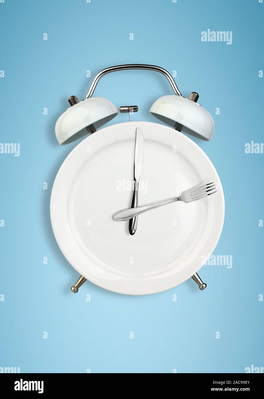 Concept of intermittent fasting, diet and weight loss. Plate as Alarm clock on blue Stock Photo