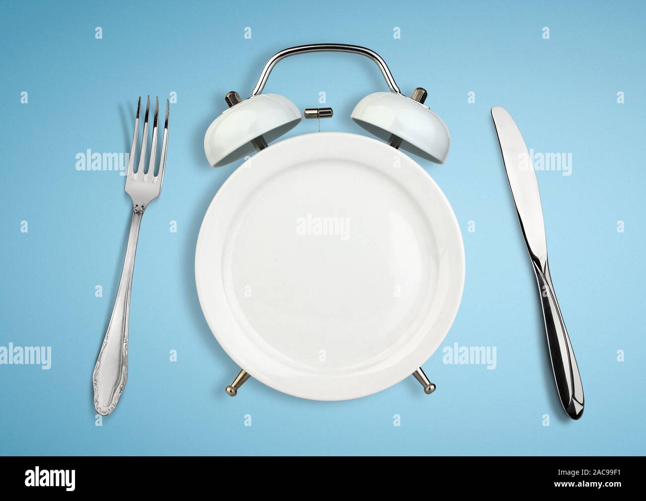 Concept of intermittent fasting, diet and weight loss. Plate as Alarm clock on blue Stock Photo