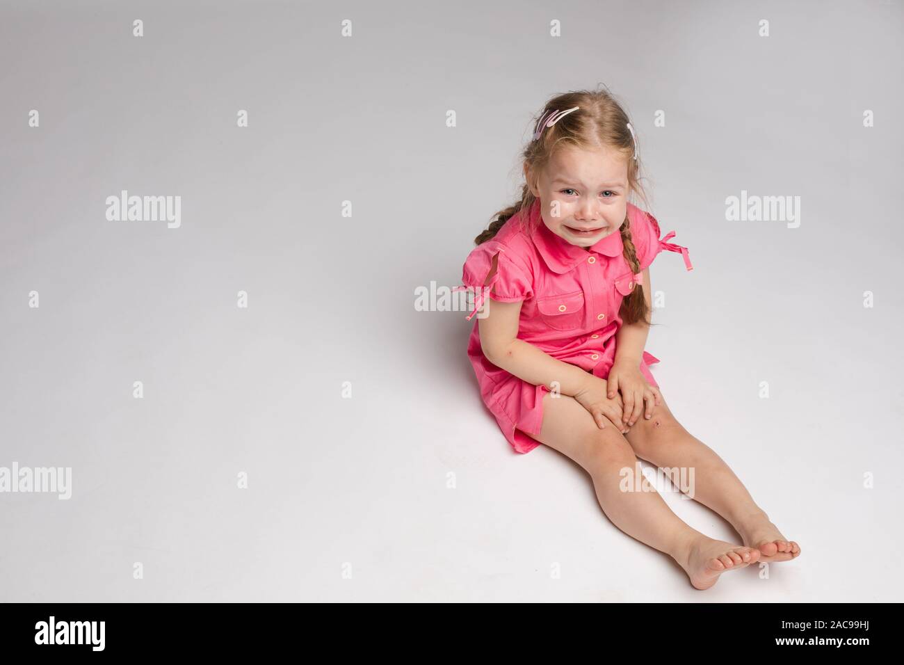 Adorable kid crying on the floor. She is looking at the camera while sobbing. Stock Photo