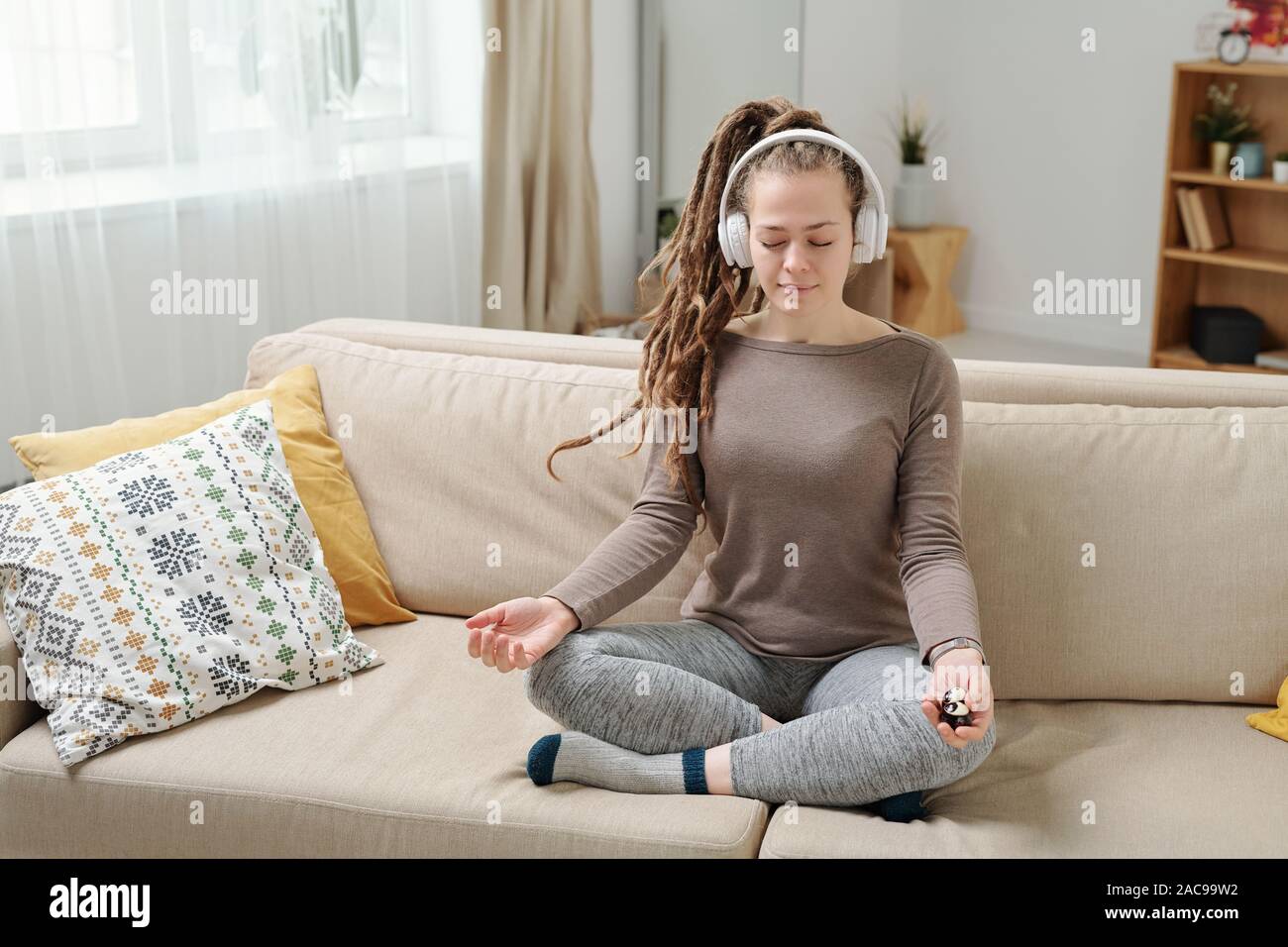 Pretty relaxed girl with antistress balls sitting in pose of lotus on couch Stock Photo