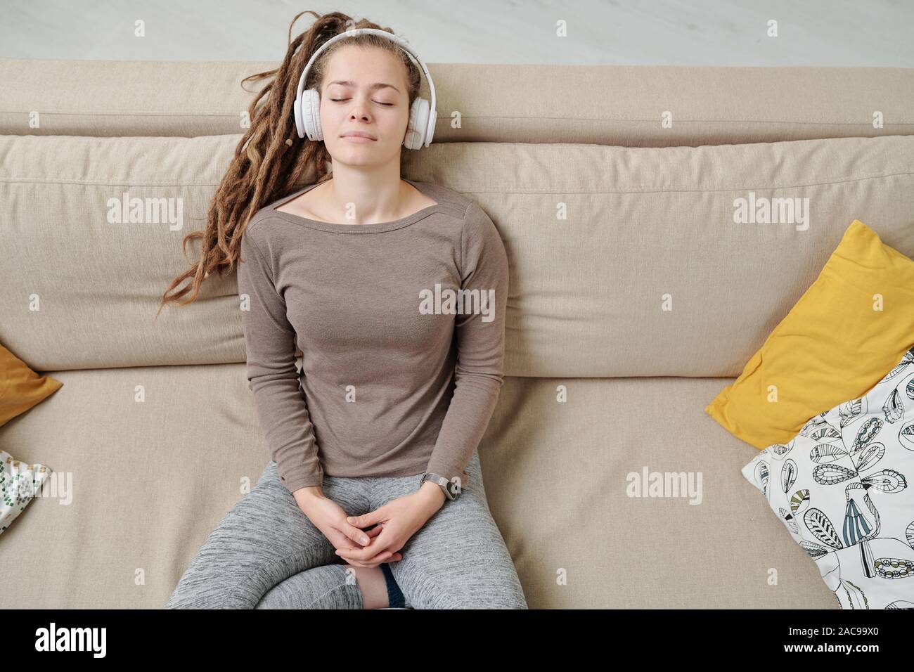 Peaceful young woman with headphones listening to meditation music on couch Stock Photo