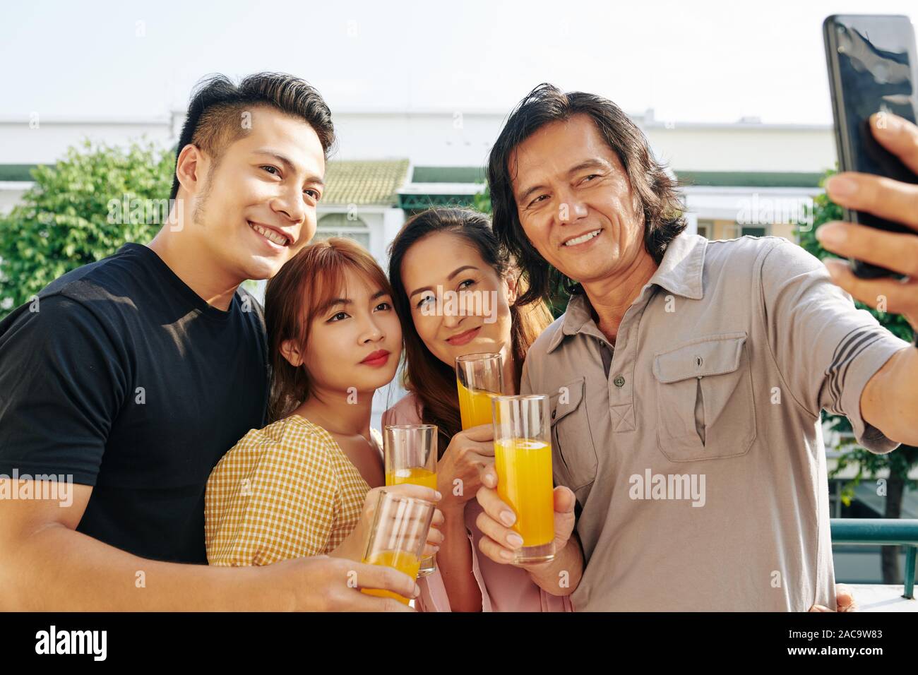 Cheerful mature Asian man taking selfie with his wife and adult children when standing on rooftop Stock Photo